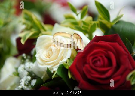 Un primo piano di due anelli di nozze su rose bianche e rosse Foto Stock