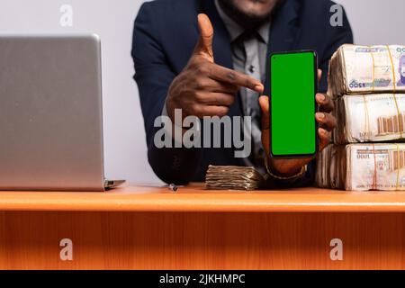 uomo d'affari africano che mostra il suo schermo del telefono accanto a un sacco di soldi Foto Stock