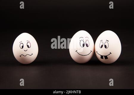 Un primo piano di tre uova bianche con facce divertenti e felici su una superficie nera Foto Stock