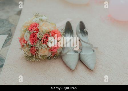 Un primo piano di scarpe da sposa e un bouquet floreale il giorno del matrimonio Foto Stock