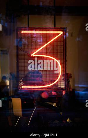 Una foto verticale di un segno al neon del numero tre alla vetrina di una caffetteria a Belgrado Foto Stock