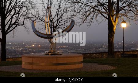 Un bellissimo scatto notturno di una moderna meridiana in un parco di Bergamo con le luci della città sullo sfondo Foto Stock