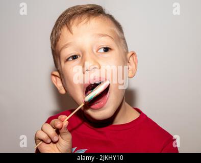 un ragazzo mangia una dolce caramella multicolore su un bastone, un ragazzo con un lecca di zucchero, che gli tiene in mano Foto Stock