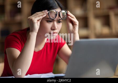 Concentrato smart teen coreana studentessa donna toglie occhiali guardare online lezione in laptop Foto Stock