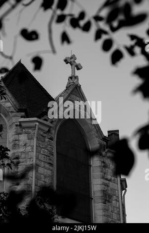 Un basso angolo scala di grigi ripresa di una croce di pietra sul campanile della chiesa contro il cielo nuvoloso Foto Stock