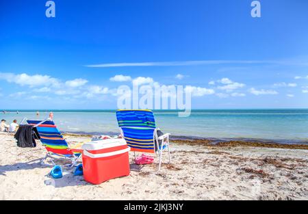 Le sedie sulla spiaggia sabbiosa sulla costa sotto il cielo nuvoloso blu Foto Stock