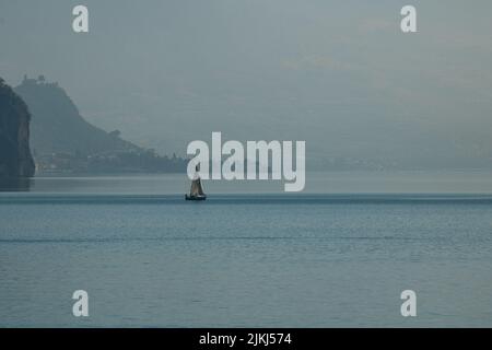 Una vista della barca che galleggia sul lago d'Iseo sullo sfondo di enormi montagne del Monte Isola Foto Stock