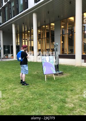 Uno scatto verticale di pittura d'arte in piedi in un cortile universitario ammirato dallo studente Foto Stock