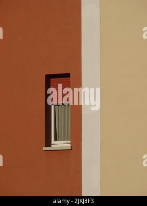 Una foto verticale di una piccola finestra bianca su un edificio arancione in una giornata di sole Foto Stock