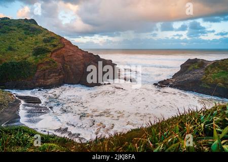 Una splendida vista panoramica della spiaggia di Piha e delle montagne contro il cielo crepuscolo al tramonto ad Auckland, Nuova Zelanda Foto Stock
