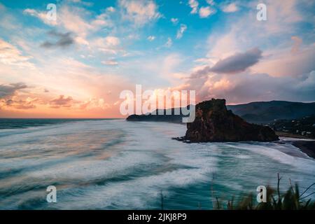 Una splendida vista panoramica della formazione rocciosa e delle montagne contro il cielo crepuscolo, Piha Beach, Auckland, Nuova Zelanda Foto Stock