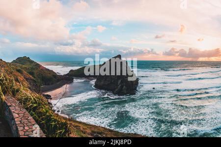 Una splendida vista panoramica della formazione rocciosa e delle montagne contro il cielo crepuscolo, Piha Beach, Auckland, Nuova Zelanda Foto Stock