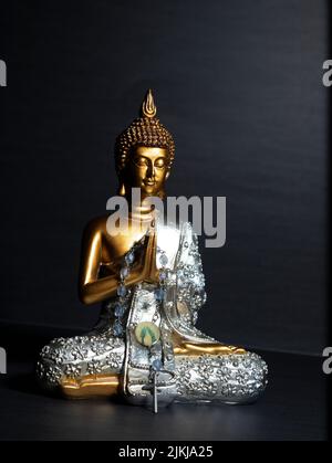 Un primo piano verticale di una statuetta dorata e argentata di Buddha su sfondo nero Foto Stock