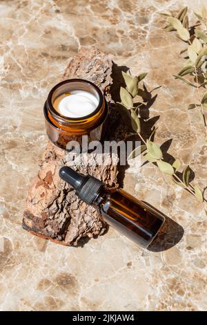 Vasetto crema idratante, siero in bottiglia di vetro su corteccia di albero. Set per prodotti di bellezza per la cura della pelle e del corpo. Confezione senza marchio con etichette vuote. Foto Stock