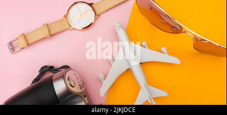 Una macchina fotografica, aeroplano, orologio e occhiali da sole su sfondo rosa e arancione Foto Stock
