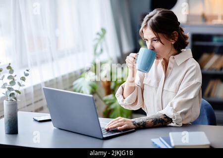 Ritratto di giovane donna tatuata che lavora da casa e bere caffè al mattino, spazio copia Foto Stock