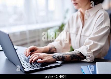 Scatto ritagliato di giovane donna tatuata utilizzando un computer portatile per il lavoro e digitando sulla tastiera, spazio copia Foto Stock