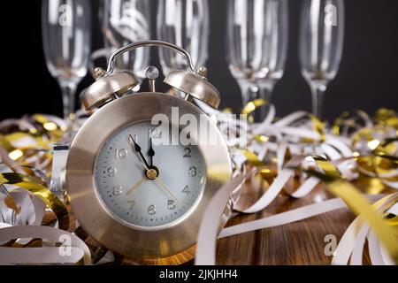 Un vetro vuoto dietro un orologio tra colorati coriandoli vicino alla parete grigia - concetto di attesa di nuovo anno Foto Stock