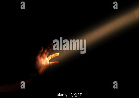Una mano che arriva per un fascio di luce su uno sfondo nero Foto Stock