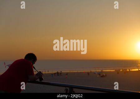 L'uomo con macchina fotografica che osserva il tramonto sul molo di Huntington Beach. Foto Stock