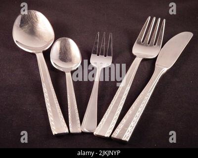 Un primo piano di coltello, forchette e cucchiai che poggiano su una tovaglia nera. Foto Stock