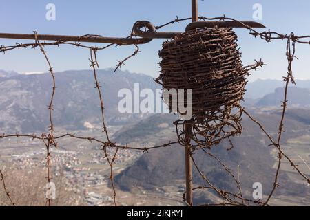 Un primo piano di un rotolo vintage di filo spinato appeso su un vecchio palo di scherma. Montagne sullo sfondo Foto Stock