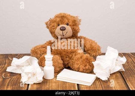 Un soffice orsetto di peluche con spray nasale e tessuti su una superficie di legno - affetto da malattia Foto Stock