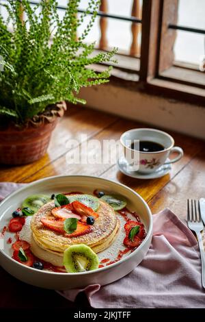 Una bella vista di frittelle dolci con frutta e una tazza di caffè su un tavolo circondato da una pianta casa Foto Stock