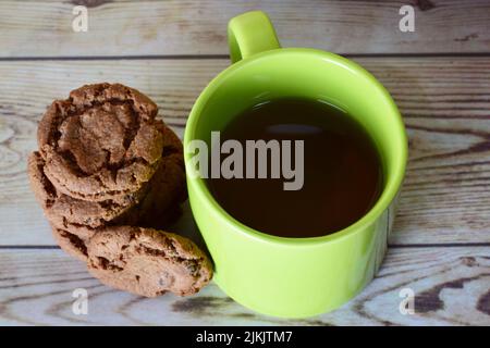 Una vista dall'alto di una tazza di tè verde accanto a biscotti impilati con scaglie di cioccolato su uno sfondo di tavolo di legno Foto Stock