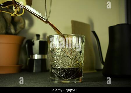 Un primo piano di caffè versato in vetro con bollitore e sacchetto di caffè sullo sfondo sfocato Foto Stock
