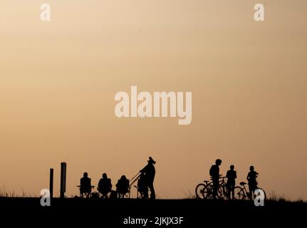 Una silhouette di una persona seduta su una sedia all'aperto e di un bambino con le biciclette Foto Stock