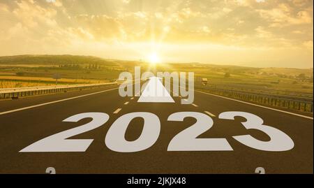 Nuovo anno 2023 concetto. Testo 2023 scritto sulla strada in mezzo alla strada asfaltata all'alba. Foto Stock