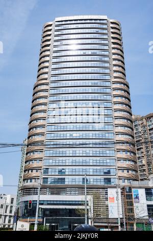 Un alto e moderno edificio con finestre di vetro che si affacciano su un cielo blu in una giornata di sole Foto Stock