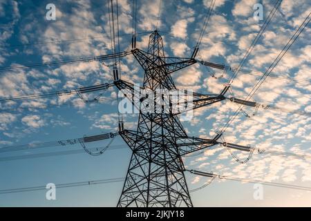 Struttura a torre tralicciata in traliccio di traliccio elettrico a tre livelli con linee elettriche aeree al tramonto nell'Inghilterra meridionale, Regno Unito Foto Stock