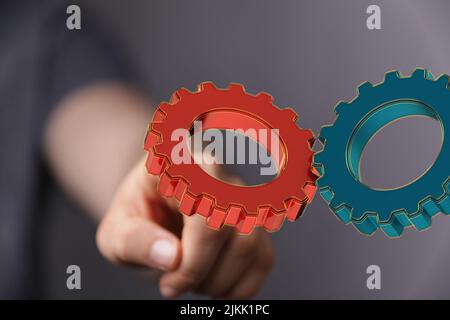 Due ingranaggi rossi e blu, su uno sfondo sfocato di una mano, come concetto di soluzione Foto Stock
