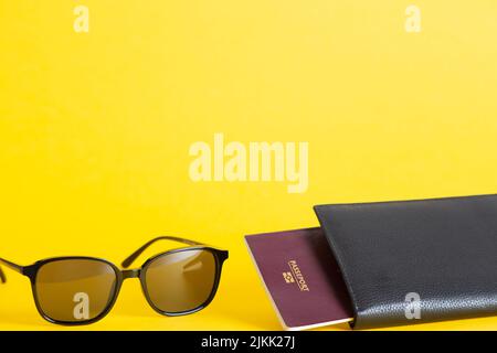 Un documento di viaggio e occhiali da sole isolati su uno sfondo giallo - concetto di viaggio Foto Stock