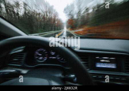 Una vista attraverso il parabrezza dell'auto su una strada forestale nella foresta sfocata in movimento Foto Stock