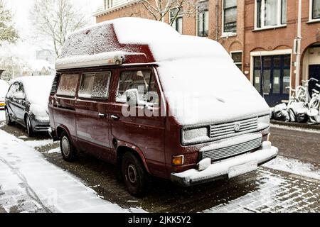 Parcheggiato furgone rosso scuro coperto di spesso strato di neve nelle strade del quartiere di Utrecht Lombok. Condizioni meteorologiche stagione inverno bianco terra urbana Foto Stock