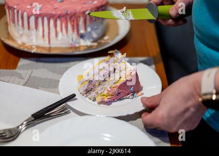 Una foto delle mani dell'uomo che tiene un pezzo di una fetta di torta di compleanno in un piatto e un coltello Foto Stock