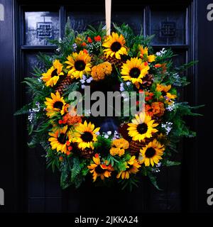 Un primo piano di una bellissima corona di girasoli appesa su una porta nera durante il giorno Foto Stock