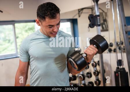 Ritratto di un uomo caucasico sportivo dai capelli scuri in palestra sollevamento pesi con un sacco di sforzo, vita sana e sana facendo sport Foto Stock