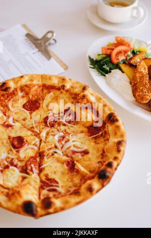 Una deliziosa pizza appena sfornata con formaggio e salsiccia e pepite di pollo con verdure sul tavolo Foto Stock