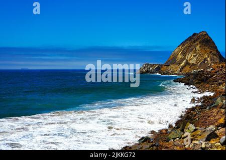 Una vista panoramica dell'oceano dalla riva - spiaggia rocciosa, onde, scogliera e cielo blu Foto Stock