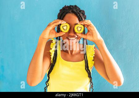Una giovane ragazza allegra di razza mista che tiene kiwi davanti ai suoi occhi Foto Stock