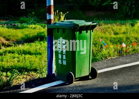 Un colpo selettivo di fuoco di un cestino pubblico verde nella strada con testo cinese sul lato Foto Stock