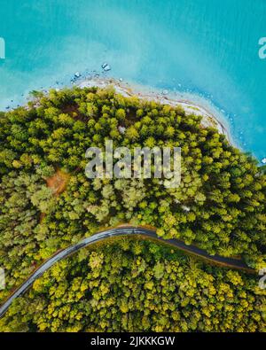 Una vista verticale del drone della strada che passa attraverso la foresta verde con un mare blu turchese Foto Stock