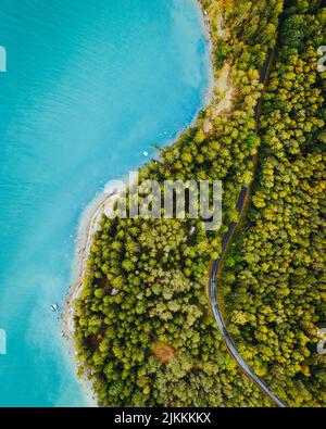 Una vista verticale del drone della strada che passa attraverso la foresta verde con un mare blu turchese Foto Stock