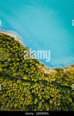 Una vista verticale del drone della strada che passa attraverso la foresta verde con un mare blu turchese Foto Stock