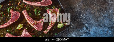 Dal panorama di sopra di costolette di agnello fresco non cotte con verde tritato posto su teglia da forno sul tavolo in cucina leggera Foto Stock