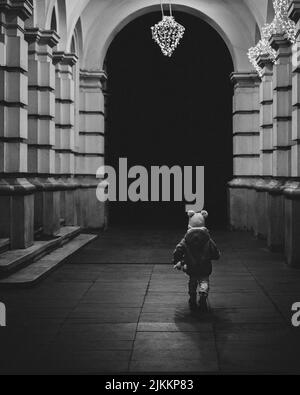 Una scala di grigi verticale di un bambino piccolo all'interno di un edificio con colonne Foto Stock